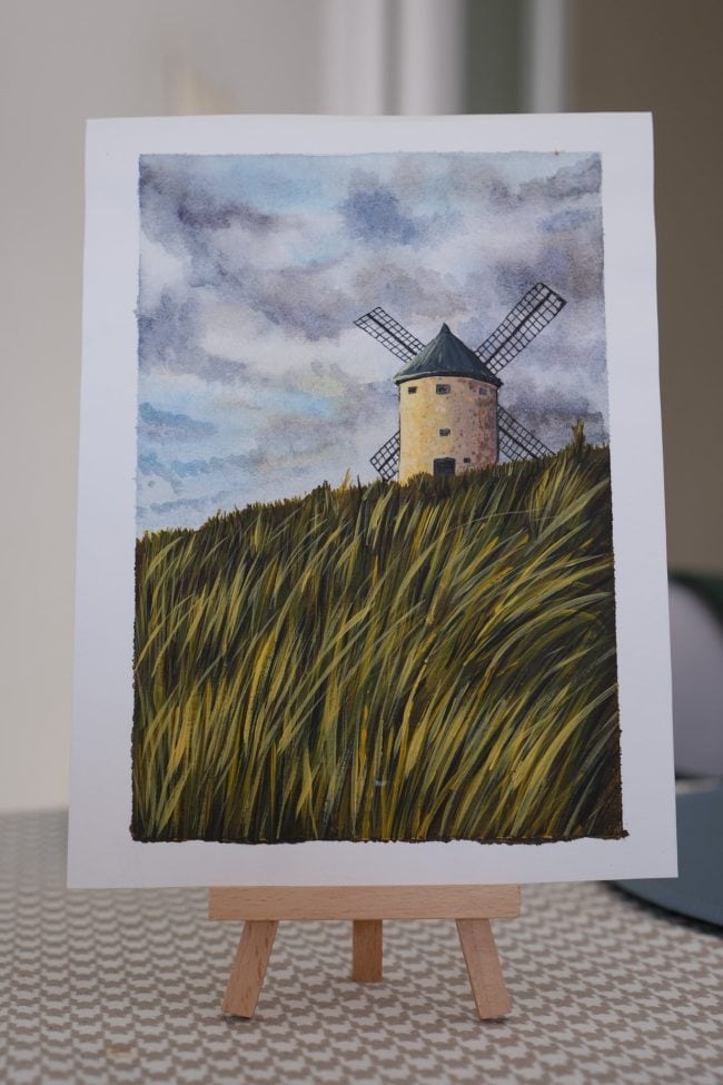 Original watercolor painting of a windmill in tall grass displayed on a small wooden easel.